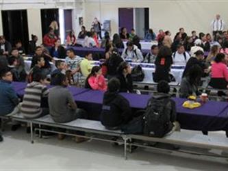 assembly of parents and students that have received honor roll awards sit at cafeteria tables eating.