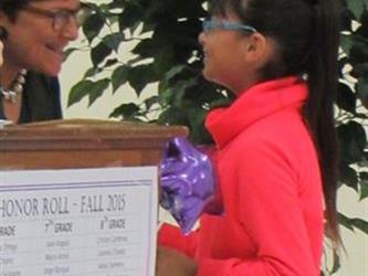 girl in pink coat with glasses receives an honor roll award.