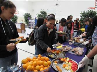 Parents and students at the buffet line serving themselves fruit.