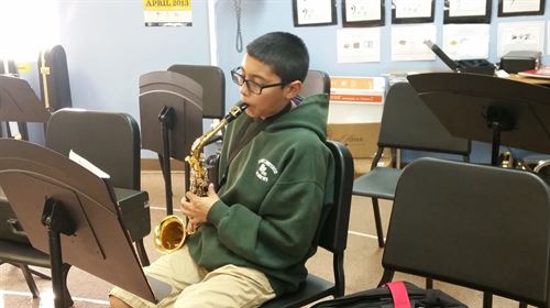 Boy sitting down and playing the alto saxophone.