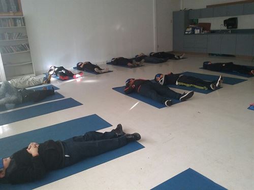 Students laying down on their backs on mats as they practice yoga.